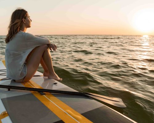 Beautiful young woman sitting on a stand up paddle board on a water